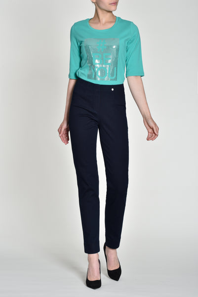 A model wearing a cropped teal t-shirt with a silver graphic print and Robell Marie 73cm navy blue slim-fit Jeans.  paired with black heels, against a light grey studio background.