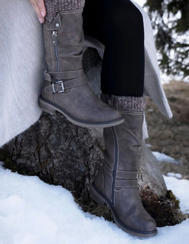 A taupe brown long boot with a knit sock-like collar, side zippers, and a buckle strap near the ankle, shown against a plain white background.