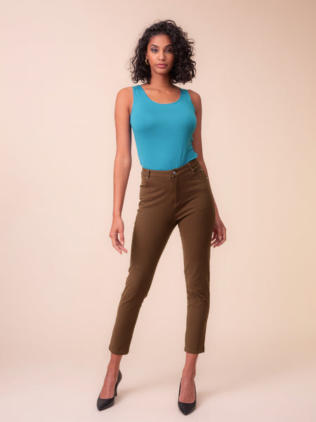 A woman modelling Alison Sheri brown slim fit Jeans with a bright turquoise sleeveless top against a solid beige studio background.