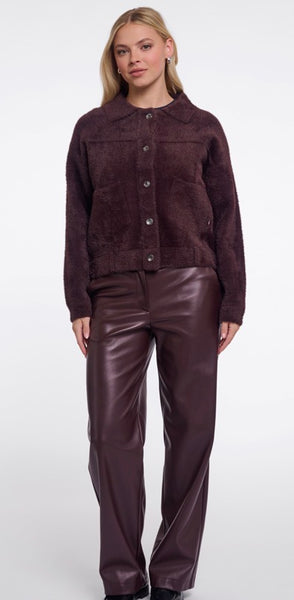 A woman modeling Rino & Pelle dark plum brown button up jacket with matching faux-leather pants against a plain white studio background.