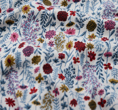 A close up of a white fabric with a dense, multicolour floral and botanical print featuring blue, pink, red, yellow, and green elements.