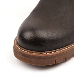 Close-up of the toe of a dark brown textured leather boot with a brown sole and light contrast stitching, shown on a white background.