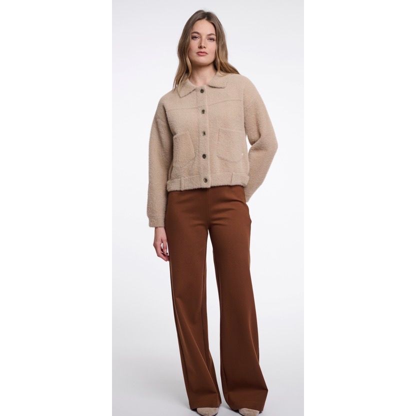 A woman modelling a Rino & Pelle cropped beige button-front jacket with front patch pockets, paired with brown wide-leg trousers, against a plain light grey studio background.