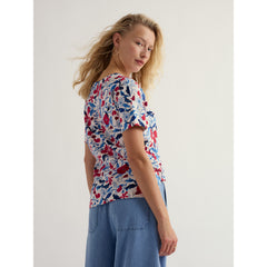 Woman wearing a colourful floral top and blue pants on a plain background.