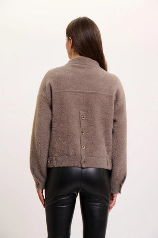 A woman viewed from the back wearing a taupe-brown cropped Rino Pelle jacket with a button closure and black faux-leather pants, against a plain white studio background.