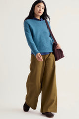 A woman modelling Seasalt blue knit sweater, olive green wide-leg trousers, and a dark brown shoulder bag against a plain light background.