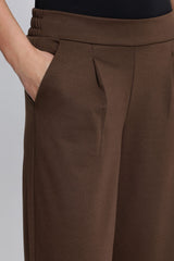 Close up of a person wearing Ichi brown wide leg trousers with a gathered elastic waistband and side pockets, paired with a black top against a light grey studio background.