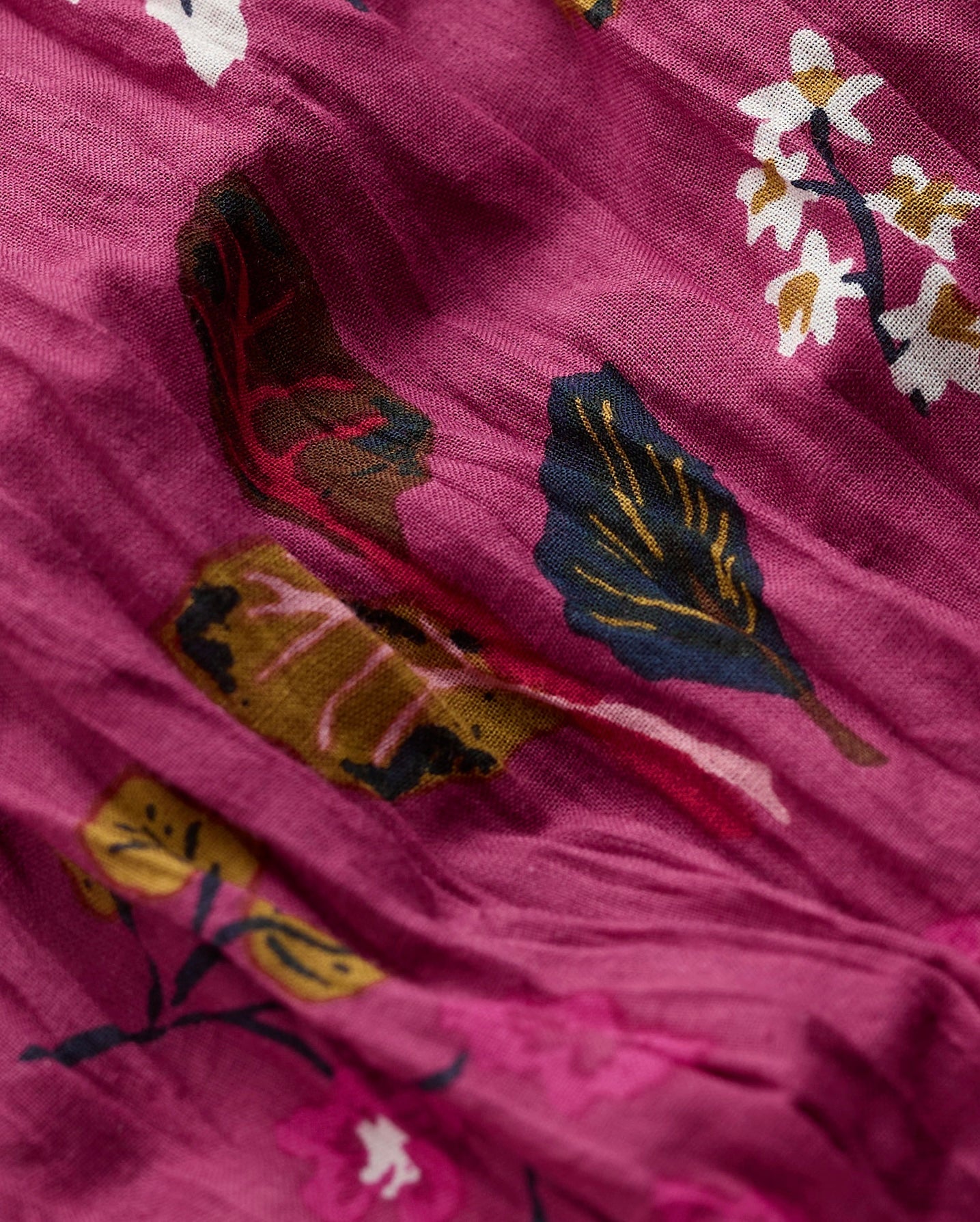 A close-up of a dusty magenta fabric with a printed botanical pattern featuring navy blue, mustard yellow, and white leaves and flowers.
