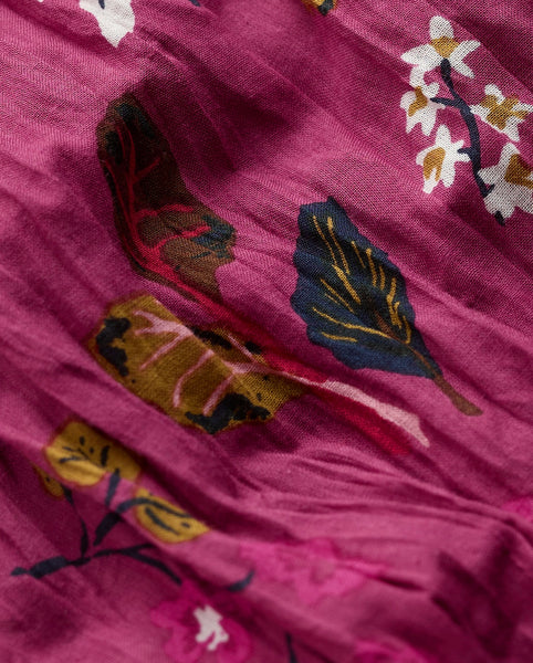 A close-up of a dusty magenta fabric with a printed botanical pattern featuring navy blue, mustard yellow, and white leaves and flowers.