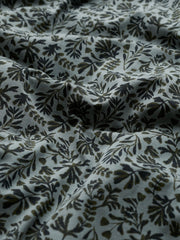 A close-up of draped fabric with an all-over botanical leaf pattern in dark olive green and black on a light gray background.