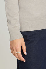Close-up of a person wearing a light beige roll neck sweater and dark navy pants, with a delicate silver ring on one finger.