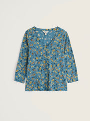 Seasalt 3/4 sleeve button front top in a dusty blue fabric with a dense yellow and orange floral print, laid flat against a light beige background.