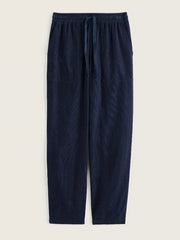 A pair of dark navy blue trousers with an elastic waistband and drawstring, displayed flat against a light beige background.