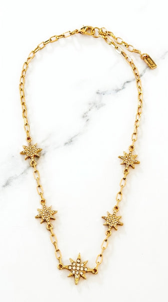 Envy Jewellery gold chain necklace featuring five starburst charms, with one larger starburst pendant embellished with small clear crystals, displayed on a white marble background.
