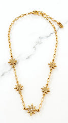 Envy Jewellery gold chain necklace featuring five starburst charms, with one larger starburst pendant embellished with small clear crystals, displayed on a white marble background.