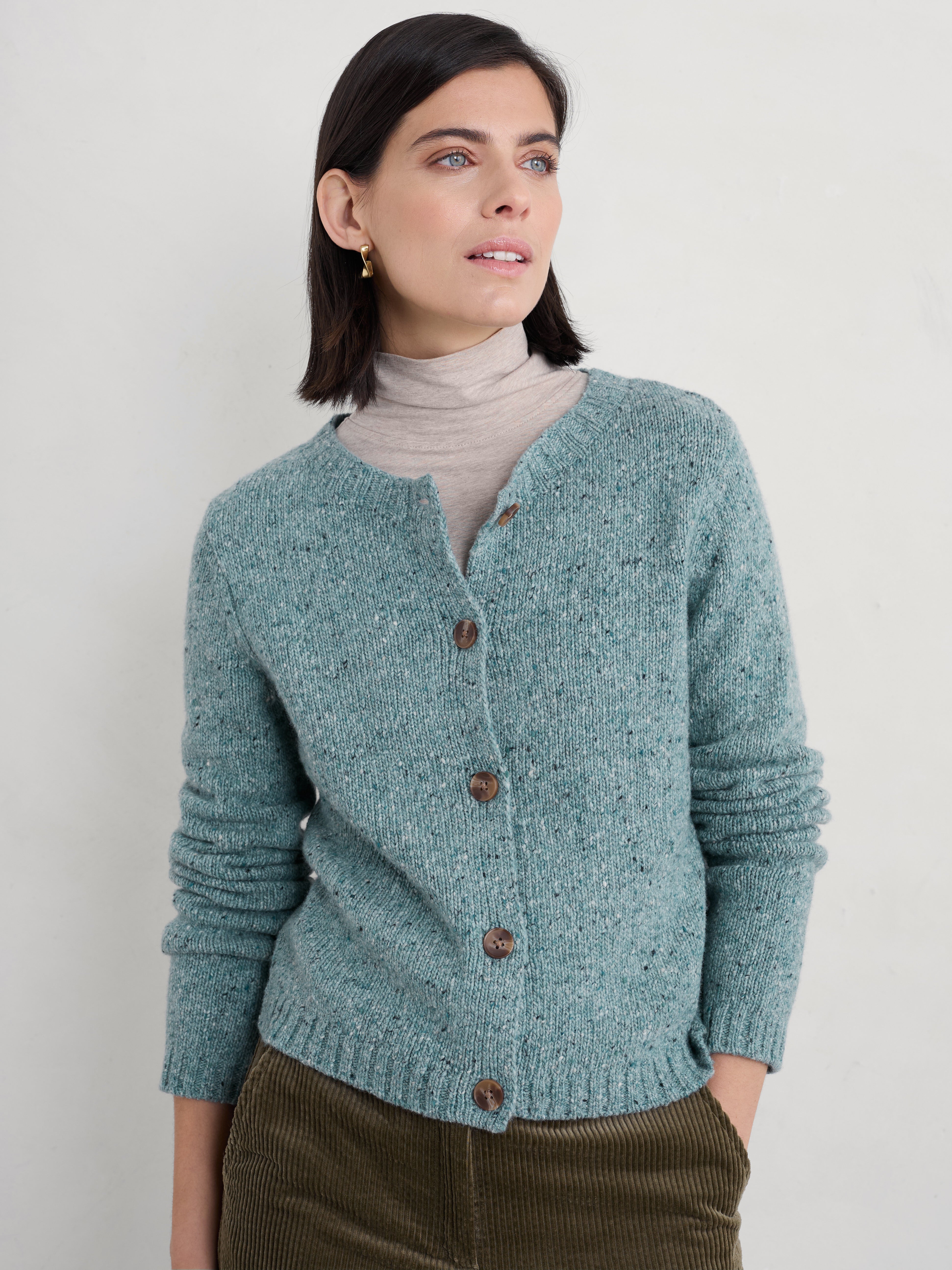 Woman wearing a Seasalt teal knitted cardigan against a plain background