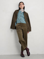 Woman wearing a Seasalt teal coloured cardigan brown jacket and green pants against a white background