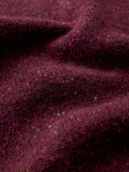 A close-up of draped dark plum tweed fabric with visible flecks and a soft, textured surface.