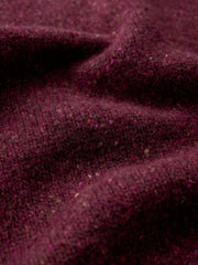 A close-up of draped dark plum tweed fabric with visible flecks and a soft, textured surface.