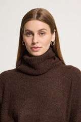 A woman with long light brown hair wearing a Ichi dark brown ribbed knit turtleneck sweater against a light grey studio background.