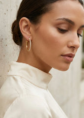 Close-up of a woman wearing Envy gold hoop earrings with a neutral background