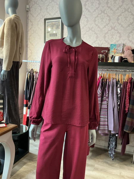 A two-piece matching lounge set in a deep berry red colour featuring an ichi long-sleeve top with a drawstring neckline and Ichi matching wide-leg trousers, displayed on a mannequin in a clothing boutique.