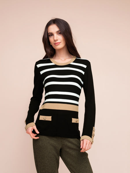 A woman modeling a black long-sleeve knit sweater with horizontal white stripes, beige trim at the collar, cuffs, and hem, paired with olive green pants against a solid beige background.
