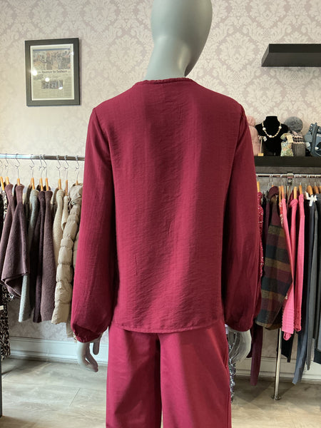 A mannequin wearing a matching two-piece lounge set in a dusty rose or deep pink color, photographed from the back inside a clothing boutique. The set includes an ichi long-sleeve top and Ichi wide-leg pants, with racks of other garments visible in the background.
