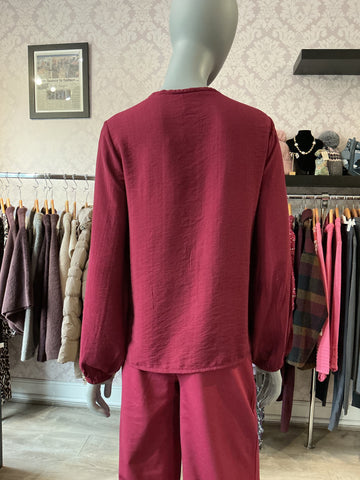A mannequin wearing a matching two-piece lounge set in a dusty rose or deep pink color, photographed from the back inside a clothing boutique. The set includes an ichi long-sleeve top and Ichi wide-leg pants, with racks of other garments visible in the background.