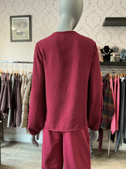 A mannequin wearing a matching two-piece lounge set in a dusty rose or deep pink color, photographed from the back inside a clothing boutique. The set includes an ichi long-sleeve top and Ichi wide-leg pants, with racks of other garments visible in the background.