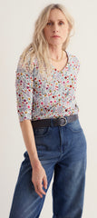 A woman modelling a Seasalt short sleeve V neck top with a dense multicolour floral and paisley print, paired with a black belt and blue jeans, against a plain light background.