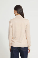A woman viewed from the back wearing a light beige Roll Neck sweater and dark blue jeans against a plain white studio background.