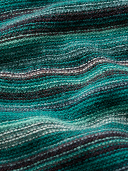 A close-up of a textured knit fabric with horizontal wavy stripes in teal, green, dark brown, and light gray.
