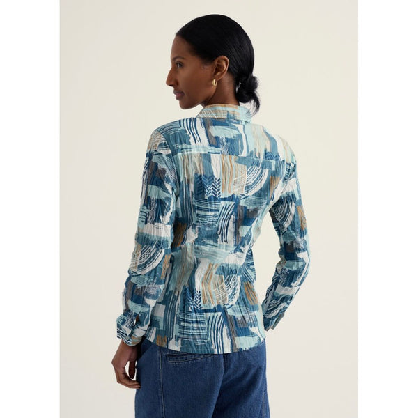 Woman wearing a patterned shirt and blue jeans on a plain background.