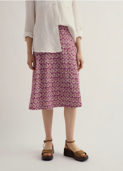 Person wearing a white top and  floral skirt on a plain background.