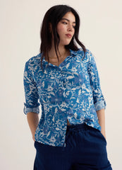 Woman wearing a blue floral blouse with navy pants on a plain background.