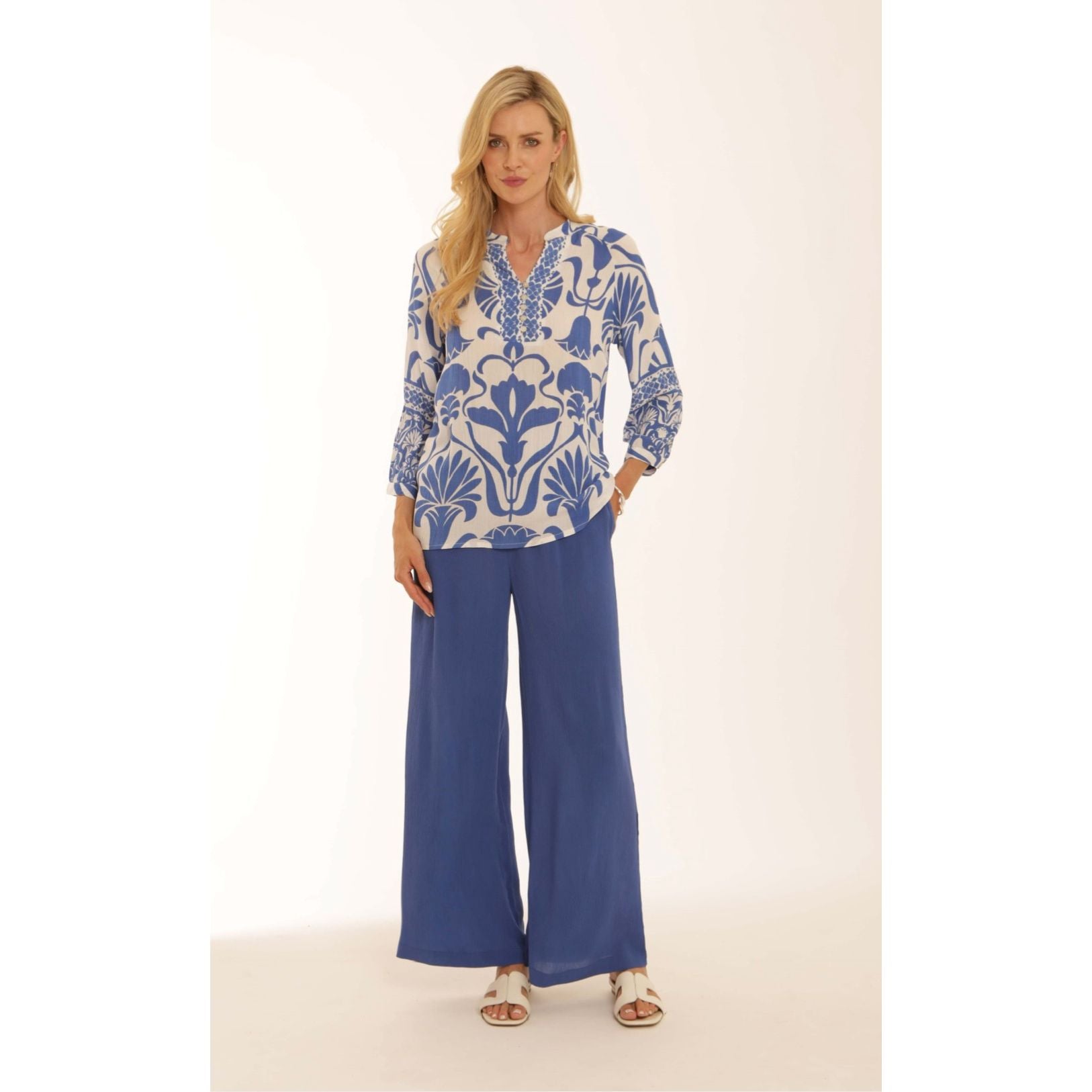 Woman wearing a patterned blouse and blue pants on a white background