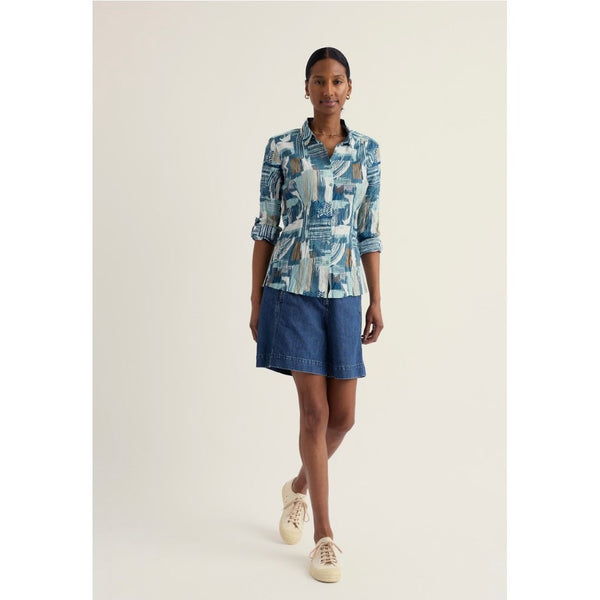 Woman wearing a patterned shirt and denim shorts on a white background.