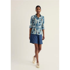 Woman wearing a patterned shirt and denim shorts on a white background.