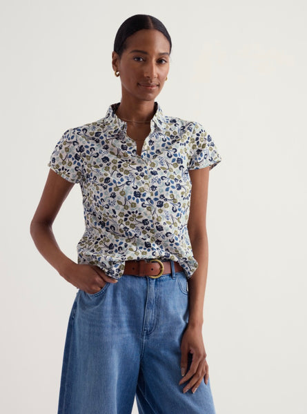 Woman wearing a floral blouse and blue jeans on a plain background.