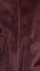 Close up of a plush faux-fur fabric in a deep brown colour, showing the soft texture and a vertical seam.