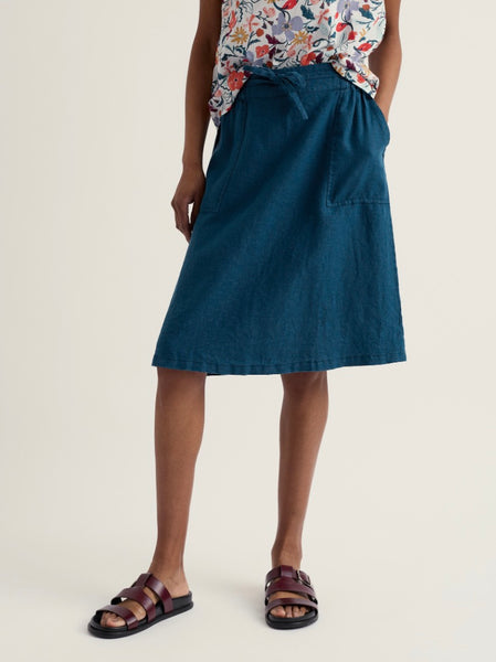 Person wearing a blue skirt and floral top on a beige background.