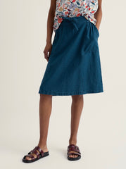 Person wearing a blue skirt and floral top on a beige background.