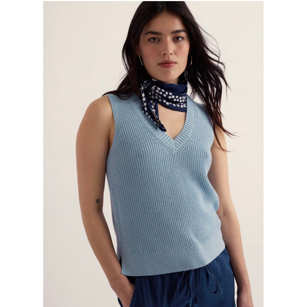 Woman wearing a light blue sleeveless sweater with a white background.