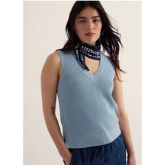 Woman wearing a light blue sleeveless sweater with a white background.