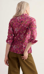 A woman shown from the back wearing a Seasalt pink floral long-sleeve blouse with pleated detailing and olive green trousers, against a plain light background.