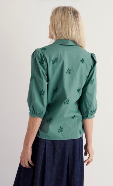 Model showing back of green embroidered 3/4 sleeve blouse worn with a blue skirt.