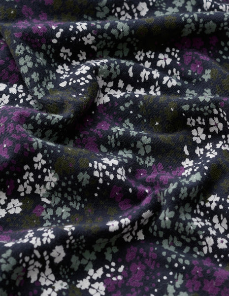 A close-up of draped fabric with a dense floral print in purple, white, and muted green on a very dark navy or black background.