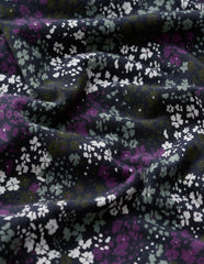 A close-up of draped fabric with a dense floral print in purple, white, and muted green on a very dark navy or black background.