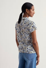 Woman wearing a floral blouse and blue jeans on a white background.